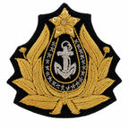 Distintivo preto em escudo com âncora prateada, estrela dourada e delicada folhagem dourada