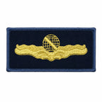 Emblema retangular azul-escuro com globo dourado bordado, linha diagonal e asas.