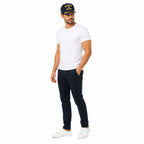 Homem com boné escuro Marinha do Brasil dourado, camiseta branca e tênis branco