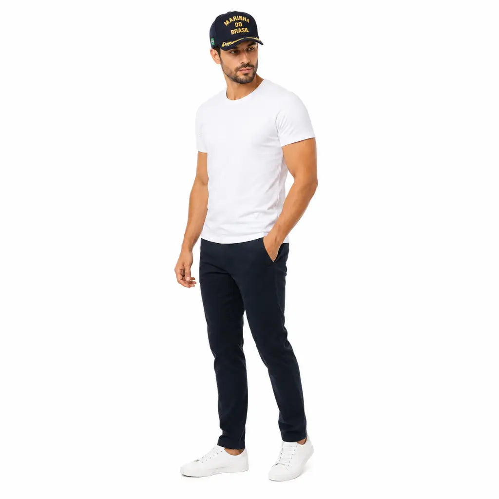 Homem com boné escuro Marinha do Brasil dourado, camiseta branca e tênis branco