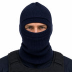 Indivíduo com balaclava azul-escuro de malha e colete tático, olhos visíveis