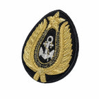 Emblema oval preto com âncora prata cercada por folhagens douradas e estrela