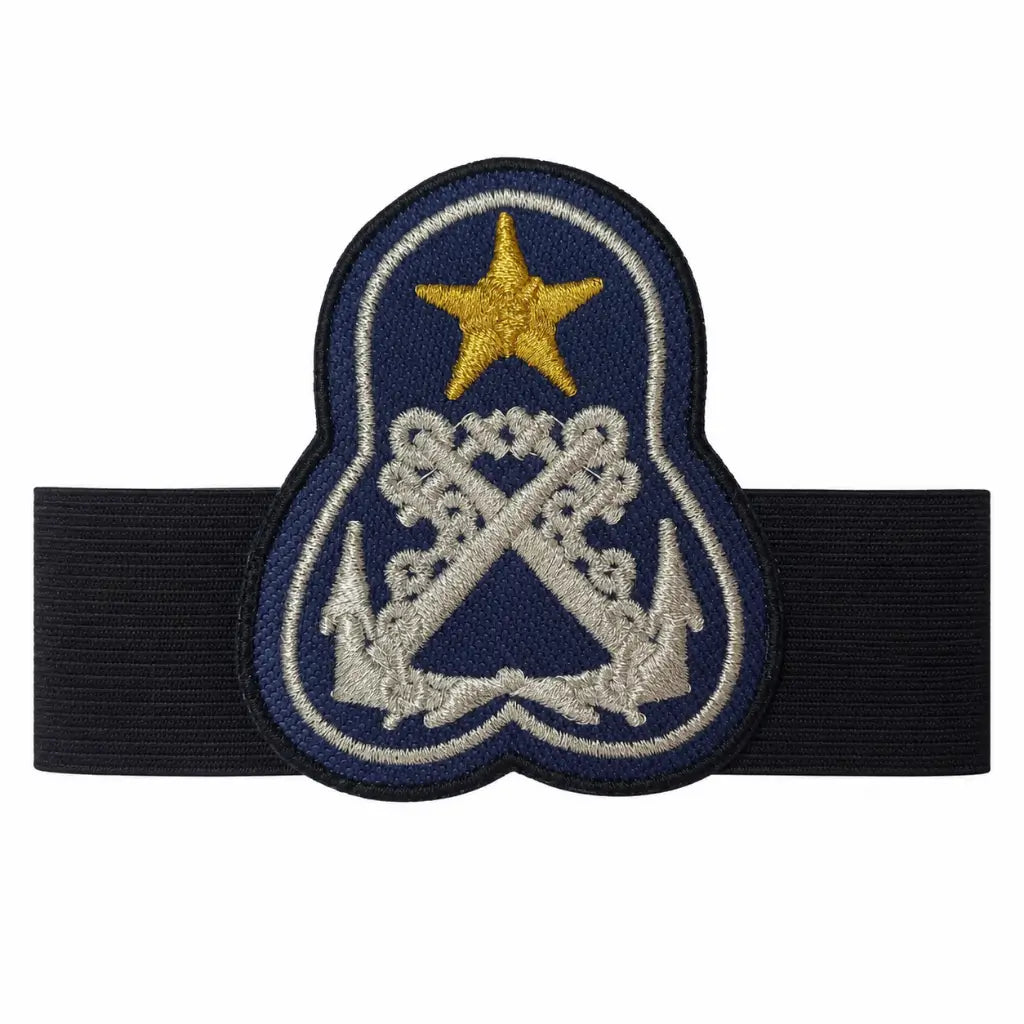 Emblema oval azul-escuro com estrela dourada e âncoras prateadas, contorno preto e faixa elástica