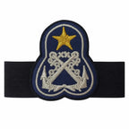 Emblema oval azul-escuro com estrela dourada e âncoras prateadas, contorno preto e faixa elástica