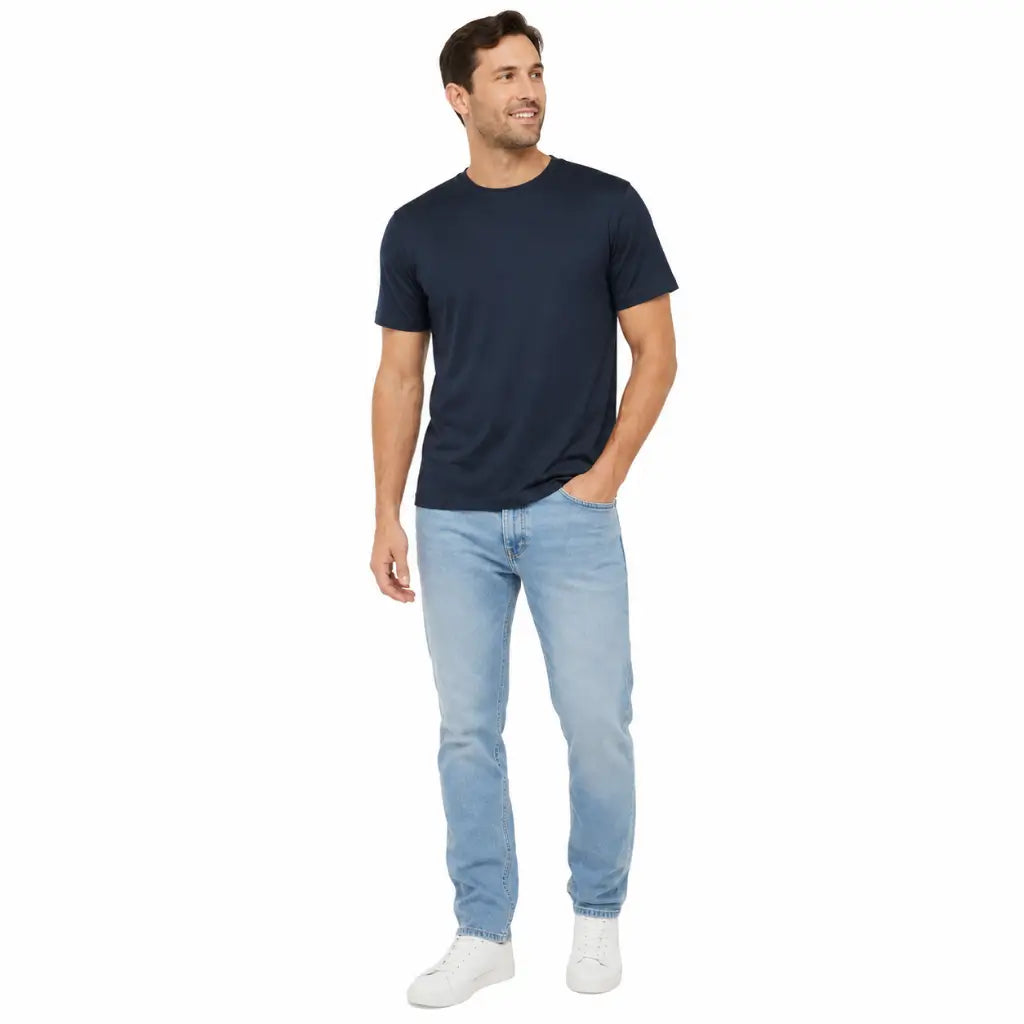 Homem sorrindo em pé com Camiseta Poliéster Marinha Marinho azul marinho e jeans claro, tênis branco