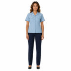 Mulher em uniforme: blusa azul clara com gola, bolsos frontais, mangas curtas, calças escuras.