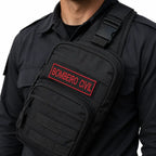 Indivíduo em uniforme preto com bolsa sling preta e patch vermelho BOMBEIRO CIVIL