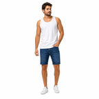 Homem em regata branca, jeans azul e tênis brancos, mãos na cintura