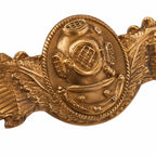 Insígnia dourada com capacete de mergulho central e ornamento em forma de ondas
