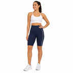 Mulher com top esportivo branco e short azul marinho com faixa lateral branca.