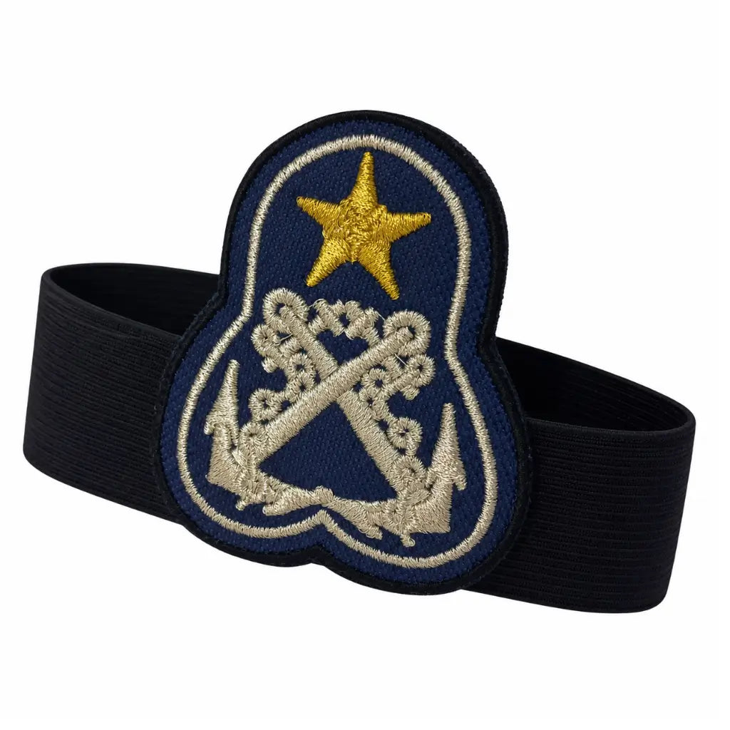 Distintivo azul escuro com estrela dourada e âncoras prateadas, preso por faixa elástica preta