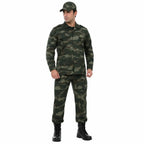 Homem em uniforme camuflado verde, boné de abas curtas, botas pretas.