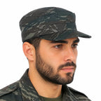 Homem com chapéu camuflado de formato quadrado e uniforme militar verde e preto.