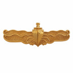 Distintivo dourado com escudo central, âncora no topo e bordas onduladas