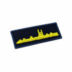 Emblema retangular preto com borda azul clara e submarino amarelo em perfil
