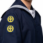 Close de uniforme naval azul marinho com dois emblemas amarelos: circular e retangular