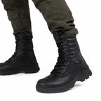 Coturno Militar Azimute Preto: close-up de botas pretas com cadarços e solado tracionado, com calça oliva