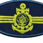 Emblema oval azul escuro com âncora amarela central, círculo atômico e duas faixas amarelas