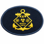 Distintivo oval azul escuro com contorno azul claro, losango amarelo, âncoras e canhões