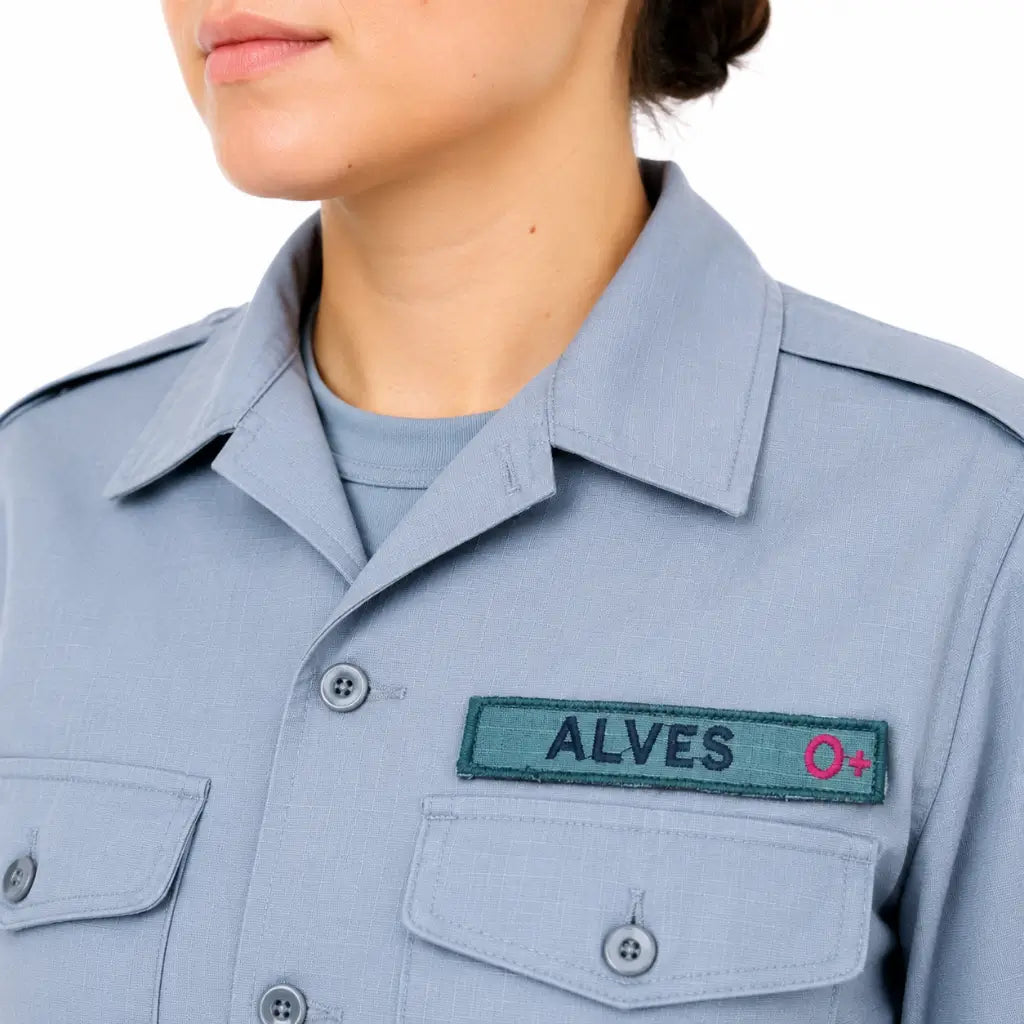 Mulher em uniforme azul claro com ALVES e O+ no peito